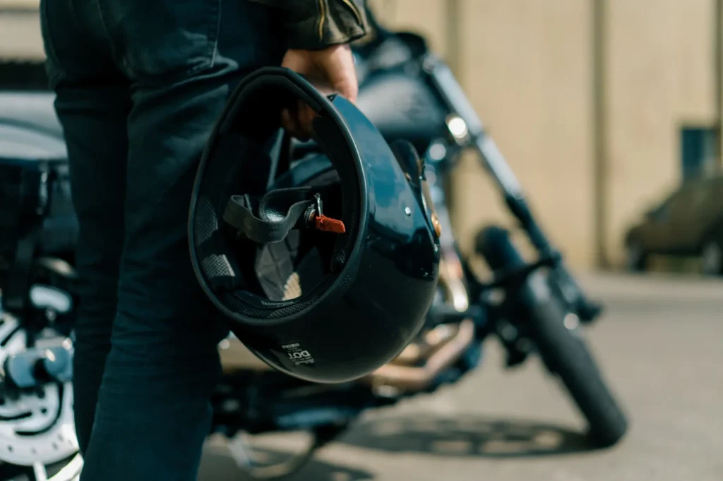 a person stands beside a motorcycle holding a helmet in their right hand ready for a ride